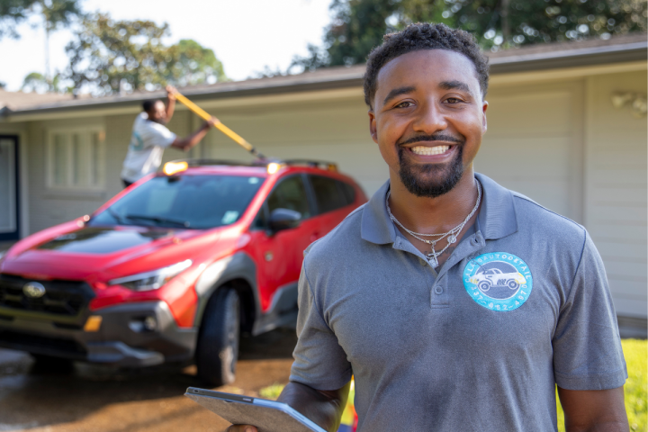 Entrepreneur Dillard Calais, graduate of UL Lafayette's online B.S.B.A. in Management program, smiles for a portrait while one of his employees details a client's car behind him.